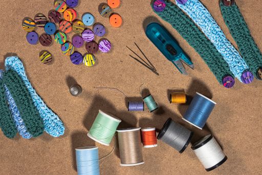 A high angle shot of small knitted belts and colorful sewing supplies on the table under the lights