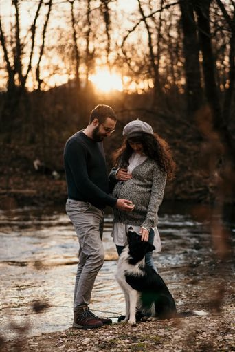 A vertical shot of a Caucasian couple with their dog doing some maternity photoshoot in the park.