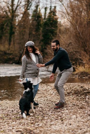 A vertical shot of a Caucasian couple with their dog doing some maternity photoshoot in the park.