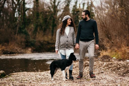 A Caucasian pregnant woman and her man walking with a dog in the park and doing some maternity photoshoot.