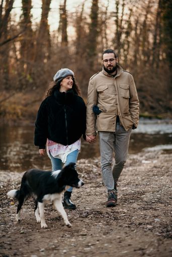 A vertical shot of a Caucasian pregnant woman and her man walking with a dog in the park and doing some maternity photoshoot.