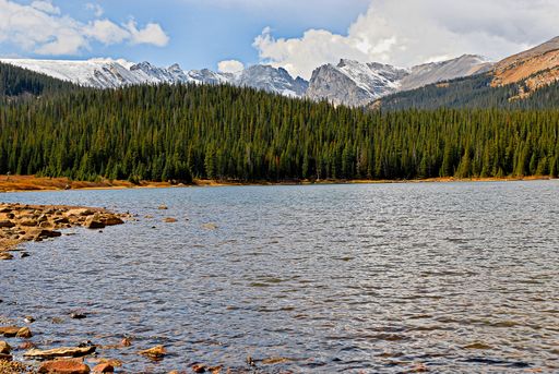 A beautiful scenery of a lake surrounded by a lot of green trees and mountains under a cloudy sky