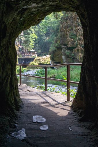 A vertical shot of a river surrounded by rocks and green trees seen through the cave