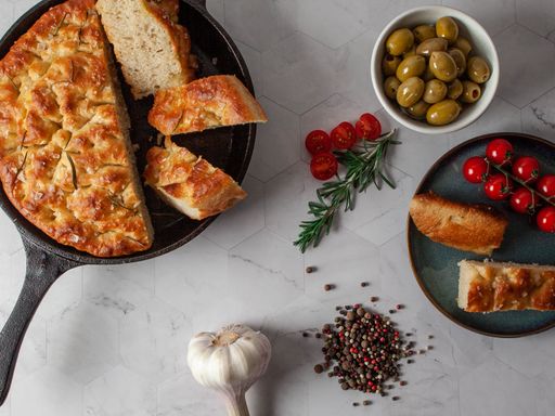 a top view of focaccia Italian bread with olive , tomato , garlic , rosemary & peppercorns on a white background