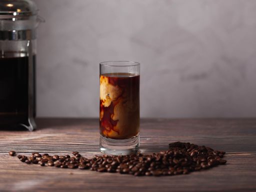 a cup of cold brew coffee surrounded by coffee beans on a woody table.