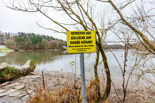 A beautiful shot of a yellow sign entering the ice at your own risk Froschgrundsee, Coburg