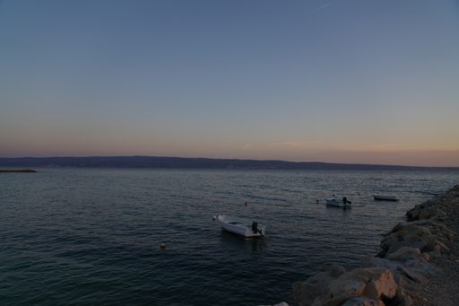 A beautiful scene of blue sea with small fishing boats near rocky shore with a colorful sunset sky