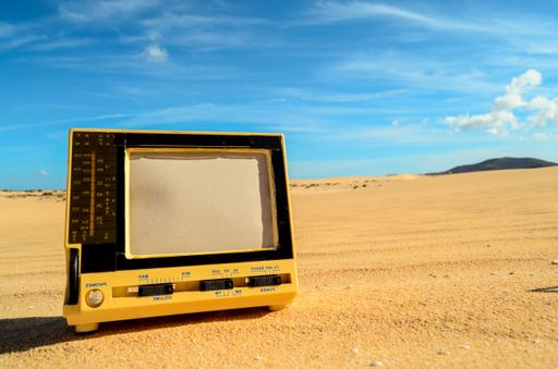 A retro television isolated on the yellow sand in the desert under a blue sky