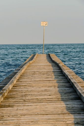 A vertical shot of a wooden pier with a signboard over the blue water under a clear sky in Morocco