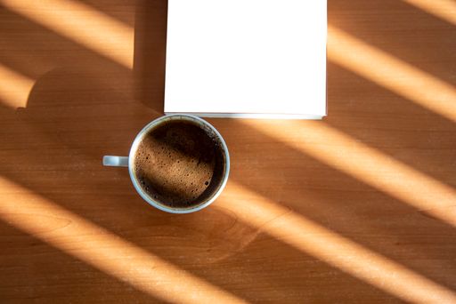 A book and a cup of Turkish coffee on a wooden table with beautiful sunlight