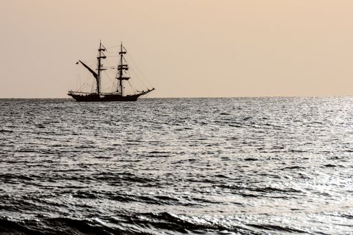 A beautiful view of bright water dunes and a silhouetted ship with a light horizon sky