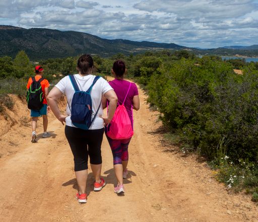 The picture shows a back view of a group of unrecognizable young people hiking on a dirt road.