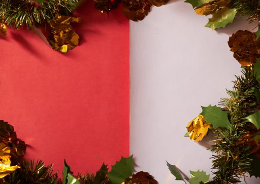 A top view of Christmas ornaments and holly leaves on a red and white surface with copy space