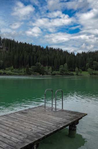 A vertical shot of a wooden jetty over the lake on a background of pine forests under a cloudy sky