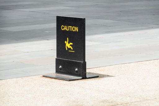 A closeup of a metal black and yellow slippery floor caution sign on the pavement under the sunlight