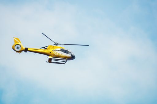 A low angle shot of a yellow helicopter flying under a blue cloudy sky in the daylight