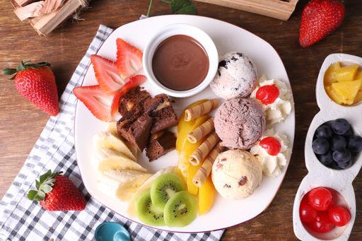 A closeup of chocolate fondue with strawberry ice cream banana waffle cherry on a white plate with tropical decoration