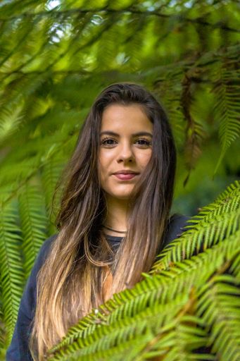 A selective focus shot of a young Caucasian brunette female covered by green leaves in the city of San Sebastian Spain