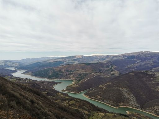 A beautiful view of a river surrounded by mountains under a cloudy sky