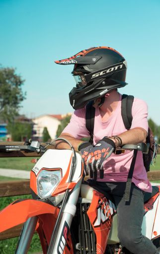 A vertical shot of a motorcyclist sitting on an orange bike, wearing a helmet and gloves