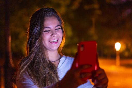 A selective focus shot of a young Caucasian brunette female using her mobile phone in the city of San Sebastian  at night