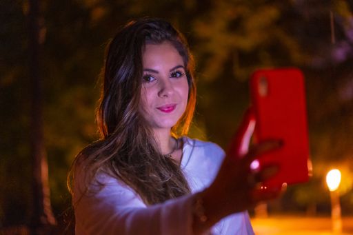 A selective focus shot of a young Caucasian brunette female using her mobile phone in the city of San Sebastian  at night