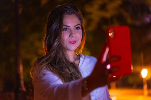 A selective focus shot of a young Caucasian brunette female using her mobile phone in the city of San Sebastian  at night