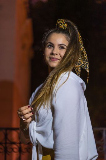 A selective focus shot of a young Caucasian brunette female wearing a hair scarf in the city of San Sebastian at night