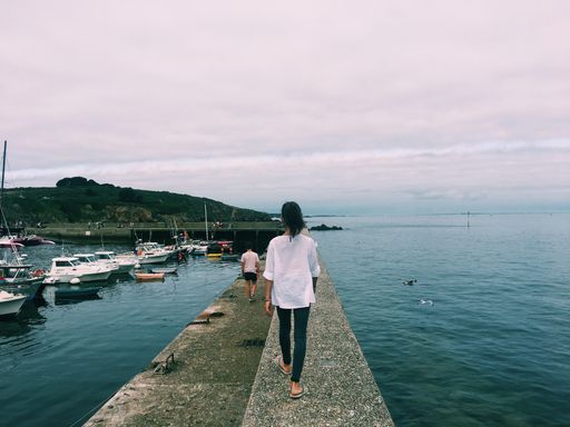 A beautiful shot of a female walking on a pathway in the middle of the sea with a mountain and a cloudy sky in the background