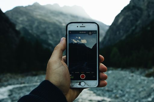 A selective closeup shot of a person holding a phone with crashed screen on the background of mountains
