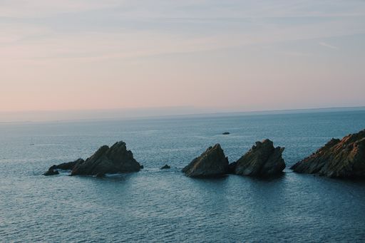 A wide shot of rock formations on the body of water under a pink sky