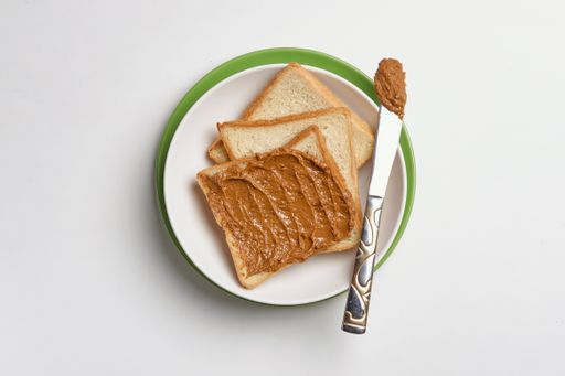 A top view of fresh toasts on the plate buttered with tasty peanut butter on the white surface