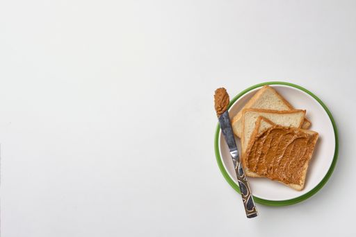 A top view of fresh toasts on the plate buttered with tasty peanut butter on the white surface