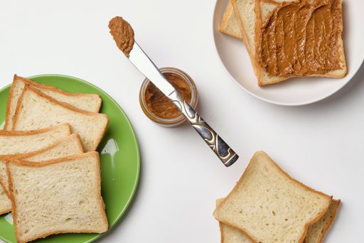 A knife on the peanut butter jar and fresh toasts on the plates over the white surface