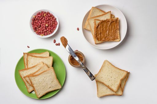 A closeup shot of peanut butter toast and peanuts on a whtie background