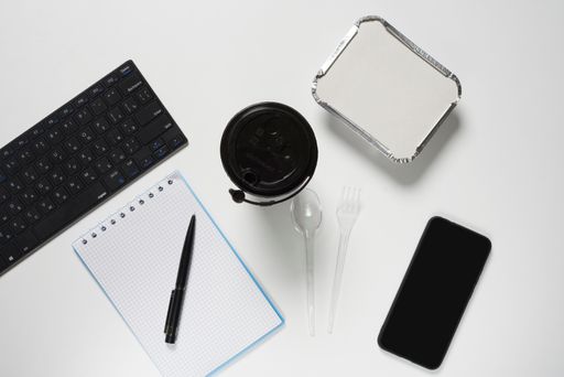 A top view shot of a keyboard, a notebook and pen and a phone on a white background