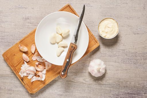 A top view of cleaned organic garlic on the cutting board and a sauce on the wooden surface