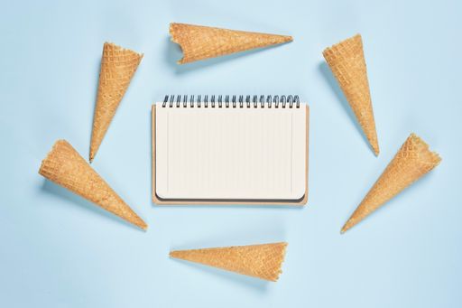 A top view shot of ice cream cones and a notebook on a blue background with copy space
