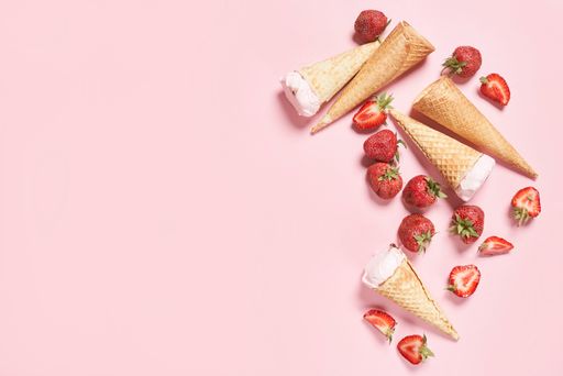 A top view of refreshing ice-creams in waffle cones and ripe strawberries over the pink surface