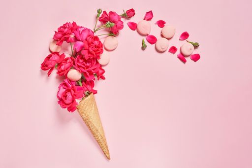 A closeup shot of an ice cream cone filled with pink petals on a pink background