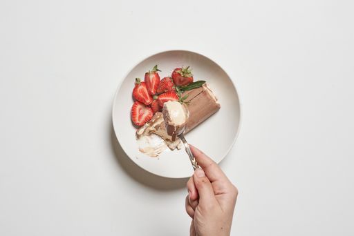 A top view of female hand taking a refreshing ice cream sandwich and strawberries on the plate
