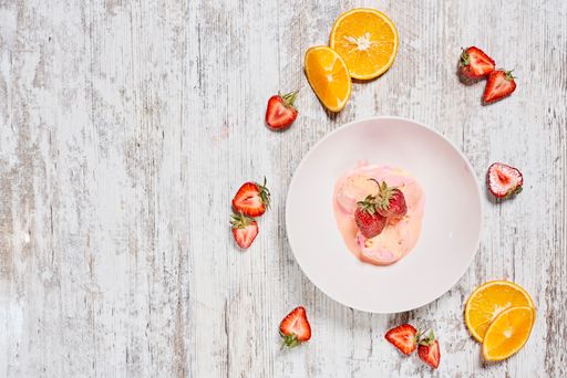 A top view shot of pink ice cream in a bowl and some fruits on a wooden background with copy space
