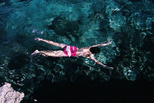 A wide shot of a person wearing pink and white swimsuit swimming in a clear sea
