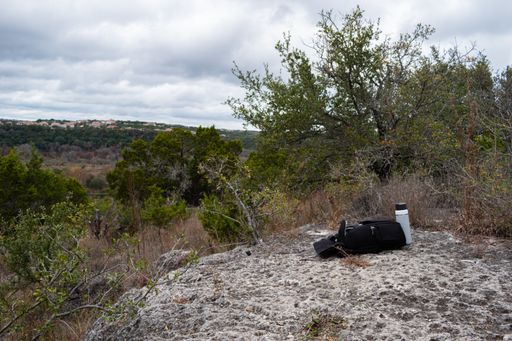 A backpack and a water bottle on a rock with a mountainous landscape in the background