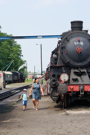A woman and child walking next to an old exhibition locomotive at an outdoor museum.