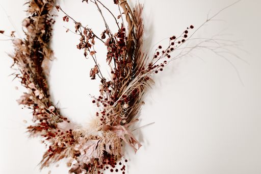A close shot of round twig wreath with leaves and red flowers on a white wall