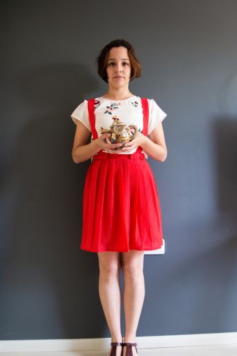 A vertical shot of a woman with a cute red dress holding a teapot