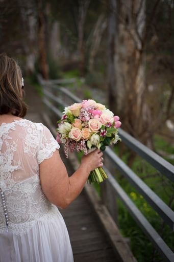 A vertical shot of a bride holding a beautiful bouquet walking on a bridge