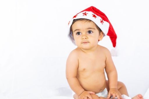 A portrait of a cute naked baby boy in a red Santa hat with stars sitting on a white background