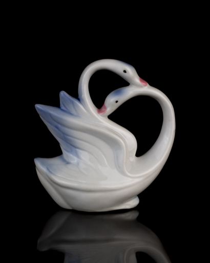 A vertical shot of a vintage small white swan statue isolated on a black background